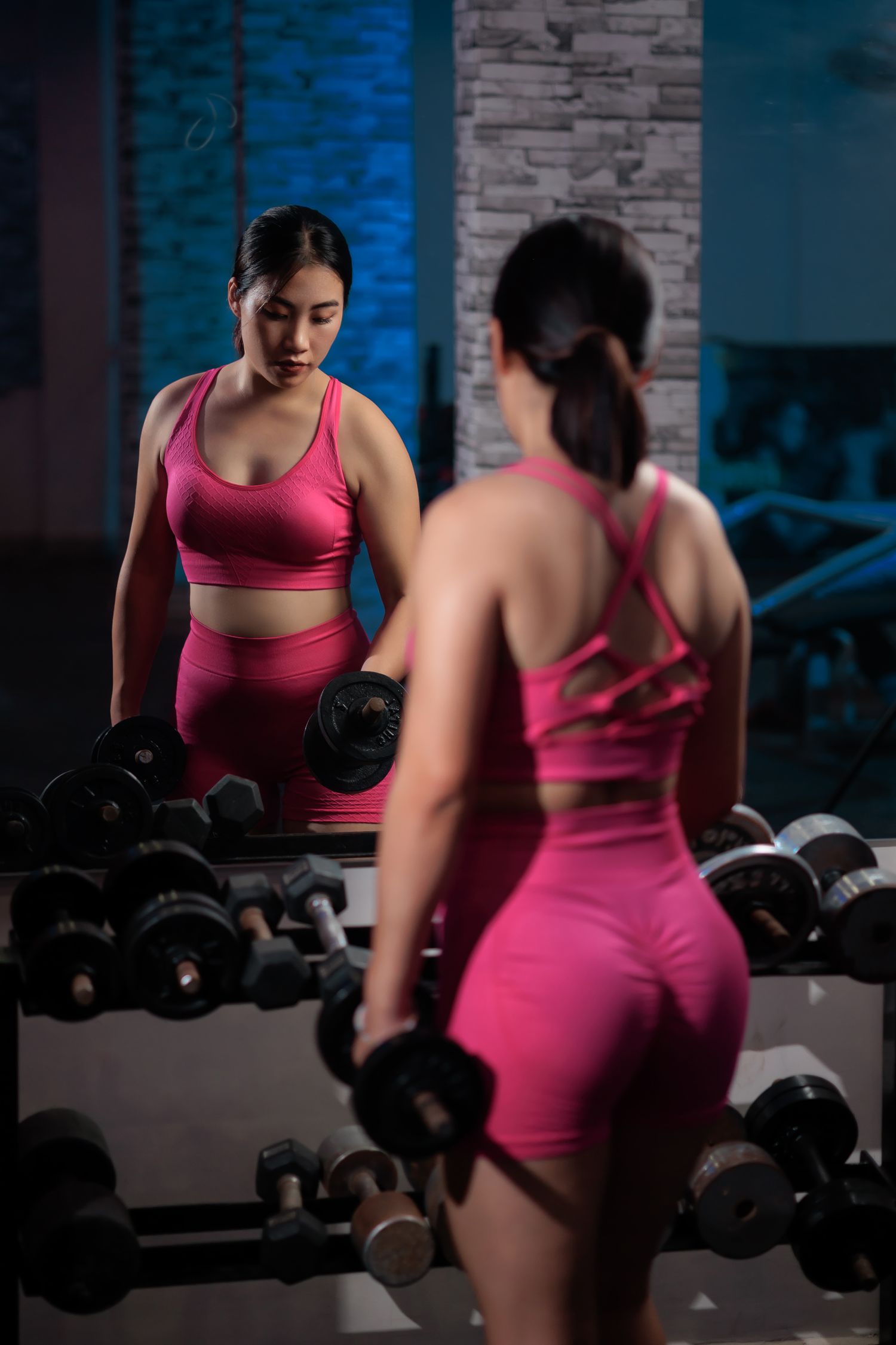 A woman in pink activewear training with dumbbells in a gym